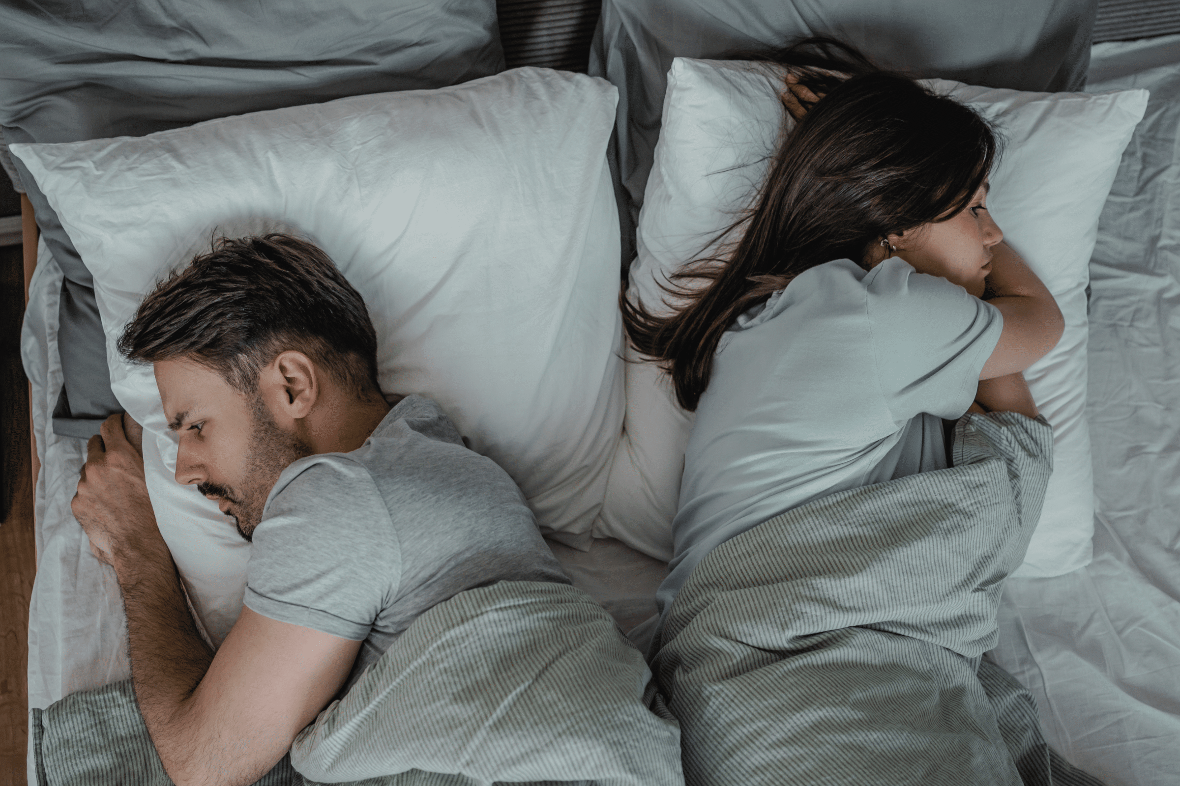 Top-down view of a couple sleeping in bed, man on the left and woman on the right under grey blankets.